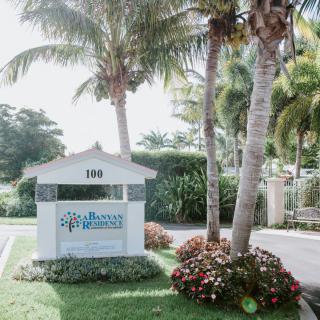Entrance sign surrounded by palm trees and landscaping.