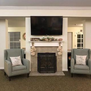 A cozy living room setup featuring a fireplace with holiday decorations, flanked by two armchairs and a television mounted above.