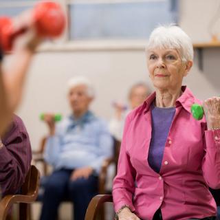 A group of seniors participating in a fitness class, lifting small weights.