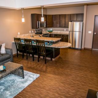 A modern open-concept kitchen and living room with hardwood floors and stainless steel appliances.