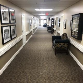 A long, carpeted hallway with seating areas and framed pictures on the walls.