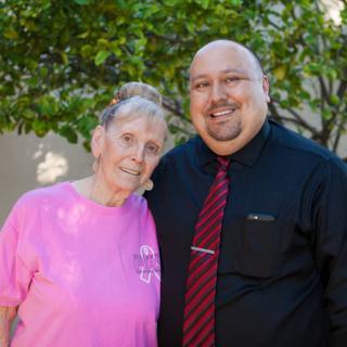 A smiling elderly woman and man standing together outdoors.