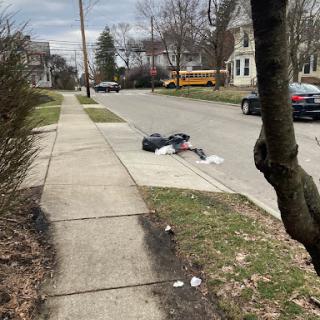 A scene on a quiet urban street featuring discarded trash on the sidewalk.