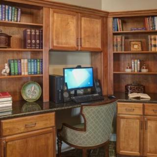 A cozy home office with a wooden desk, computer, and bookshelves filled with books.