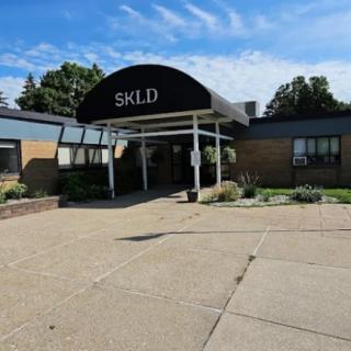 The image shows the entrance of a building with an awning labeled 'SKLD'.