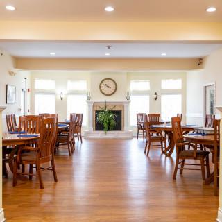 A spacious dining room with wooden tables and chairs, featuring a fireplace and large windows allowing natural light.