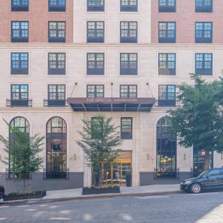 A modern hotel building with a stylish facade and tall windows, surrounded by trees in an urban setting.