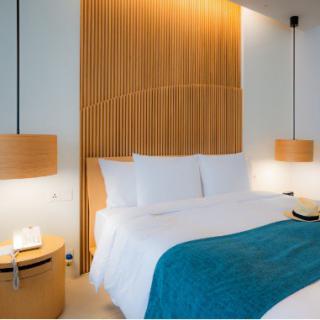 A modern hotel room with a neatly made bed, featuring blue accents and warm wooden decor.