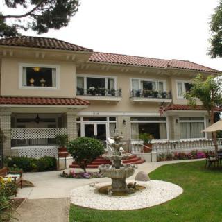 A large two-story house with a beautiful garden and fountain in the front yard.
