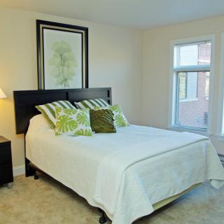 A cozy bedroom with a neatly made bed, decorative pillows, and a large window.