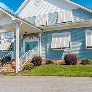 A light blue house with white trim and a manicured front yard under a bright blue sky.