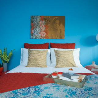A modern bedroom with vibrant blue walls and red accents, featuring elegant decorative pillows and artwork above the bed.