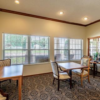 A bright dining area with tables and chairs, featuring large windows and decorative carpeting.