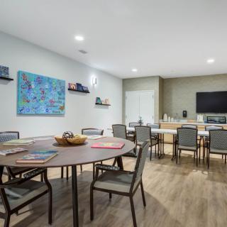 A modern meeting room with round tables and chairs, featuring a television and wall art.