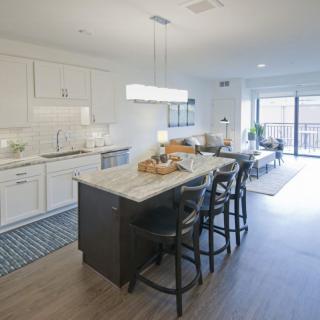 A modern open-concept kitchen with a central island and dining area, featuring bright lighting and wood flooring.