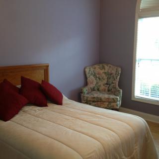 A cozy bedroom with a neatly made bed and an accent chair by the window.