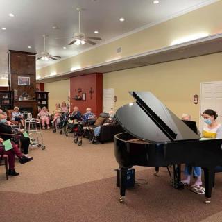 A pianist performs in front of an attentive audience in a cozy indoor setting.