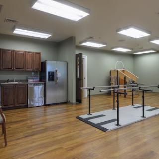 A spacious physical therapy room equipped with exercise bars and a kitchen area.