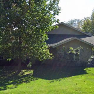 A residential house surrounded by a lush green lawn and a large tree under bright sunlight.