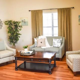 A cozy living room with a sofa, armchairs, and a coffee table, decorated with throw pillows and an indoor plant on a hardwood floor.
