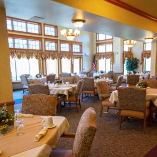 A cozy dining area in a restaurant with neatly arranged tables and chairs, large windows, and soft lighting.