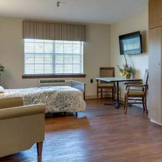 A cozy bedroom with a bed, chairs, table, and a wall-mounted TV.