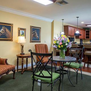 A cozy living room with a small dining table, surrounded by comfortable seating and decorated with paintings and fresh flowers.