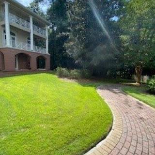 A large house with a well-manicured lawn and a brick driveway leading towards it on a sunny day.