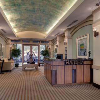 A stylish and welcoming reception area with a wooden desk, elegant ceiling design, artwork, and potted plants.