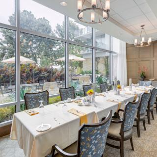 A beautifully set dining table in a bright room with large windows overlooking a garden.