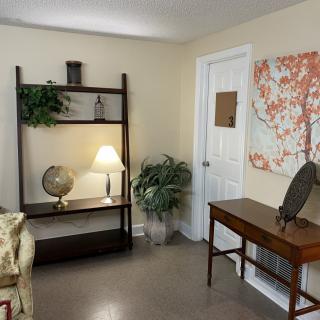A cozy living room corner with a decorative shelf, lamp, globe, and artwork on the wall.