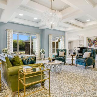 A luxurious and spacious living room featuring elegant furniture and a coffered ceiling with a modern chandelier.