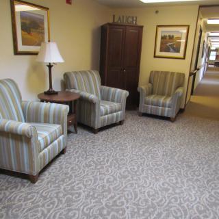 A cozy seating area in a hallway with striped chairs, a lamp, and artwork on the walls.