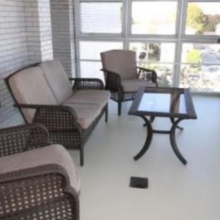 A cozy patio setup with wicker furniture and a glass-top table, surrounded by large windows.