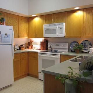 A modern kitchen with wooden cabinets, featuring a refrigerator, microwave, oven, and ample countertop space.