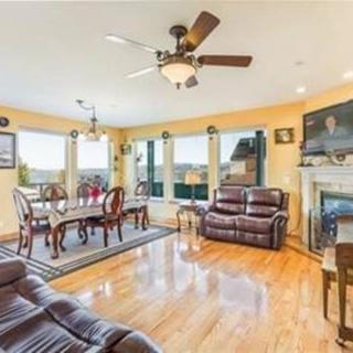 A spacious living room with hardwood flooring, featuring leather sofas, a dining area, and a cozy fireplace. Large windows allow plenty of natural light to brighten the space.