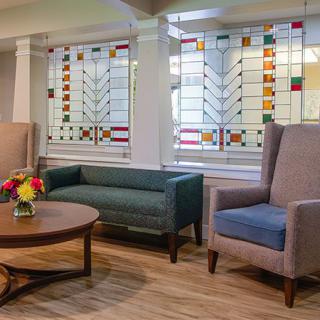 A cozy waiting area featuring stained glass windows, comfortable seating, and a coffee table with a vase of flowers.