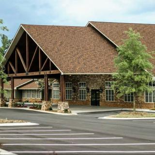 A modern building with a stone facade and a large gabled roof, surrounded by trees and an empty parking lot.