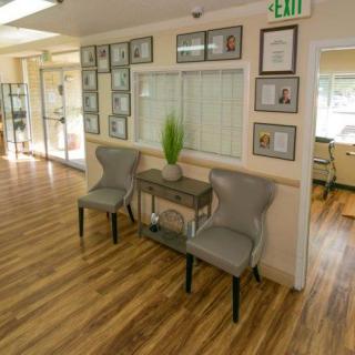 A cozy waiting area with two chairs and a small table, accented by decorative plants and framed pictures on the wall.