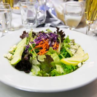 A fresh garden salad with mixed greens, sliced avocado, and shredded carrots, served on a white plate.