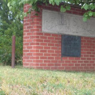 A brick structure with a plaque, surrounded by grass and trees.