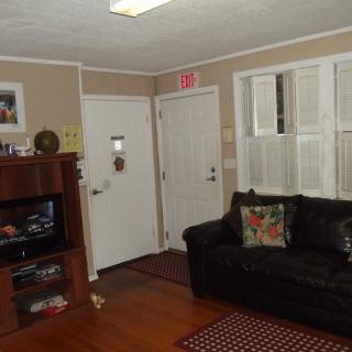 A cozy living room with a black sofa, television, and wooden flooring.