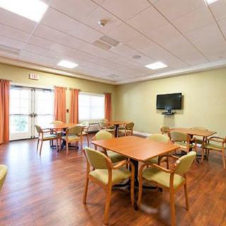 A well-lit dining area with tables and chairs, featuring a television on the wall and wooden flooring.