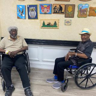 Two elderly men enjoying each other's company in a community center, surrounded by vibrant artwork.