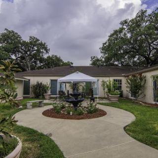 A serene courtyard featuring a circular pathway, lush greenery, and a tent for gatherings.