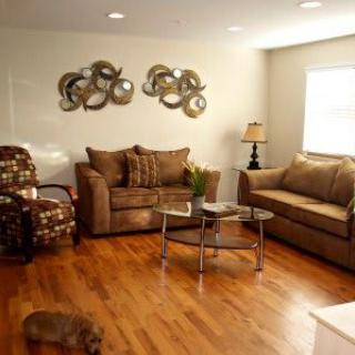 A cozy living room with brown sofas, patterned chairs, a glass coffee table, and artistic wall decor.