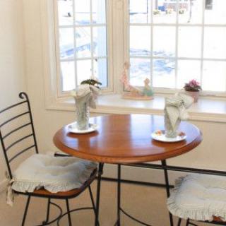 A cozy indoor seating area by a window with a round wooden table and two chairs, adorned with decorative vases and flowers.