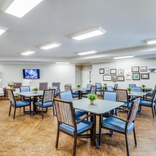 A modern dining area featuring multiple tables and chairs, decorated with potted plants, and a television mounted on the wall.