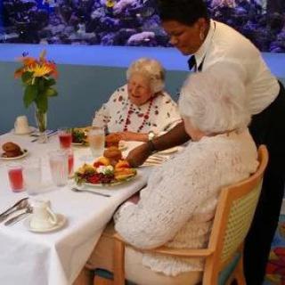 A waiter serves a meal to two elderly women seated at a dining table.