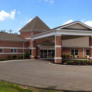 A brick building with a covered entrance and driveway surrounded by greenery under a clear sky.